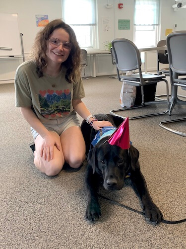 raiser Ashley with black pup Watkins in party hat on campus