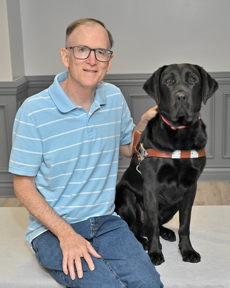 John sits with black Lab guide Gibbs for their team portrait