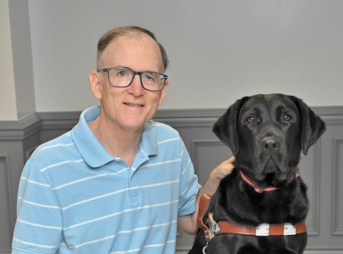 John sits with black Lab guide Gibbs for their team portrait