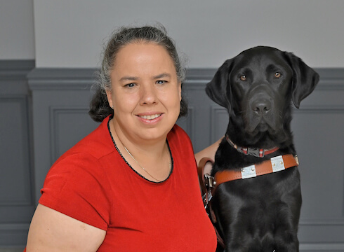 Judy sits with black Lab guide Lyons for their team portrait