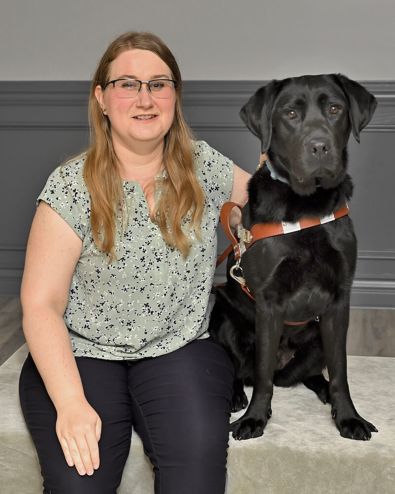 Lindsay sits with black lab guide dog Eve for team portrait