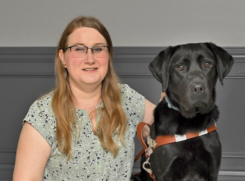 Lindsay sits with black lab guide dog Eve for team portrait