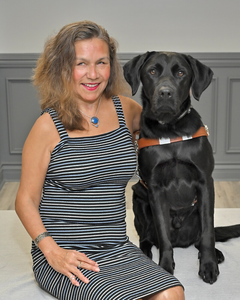 Maria sits with black lab guide dog Eve for team portrait