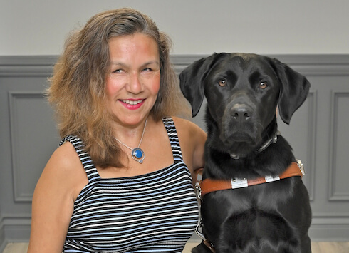Maria sits with black lab guide dog Elmer for team portrait