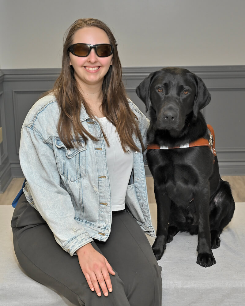 Miranda sits with black Lab Guide dog Grover for their team portrait