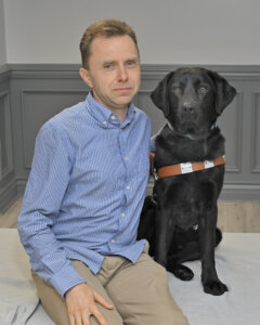 Thomas sits with black lab guide dog Kemp for team portrait