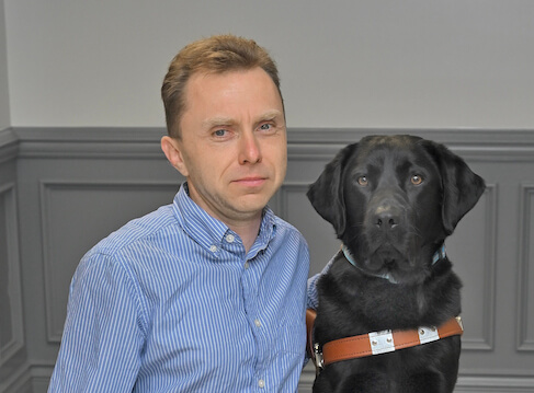 Thomas sits with black lab guide dog Kemp for team portrait