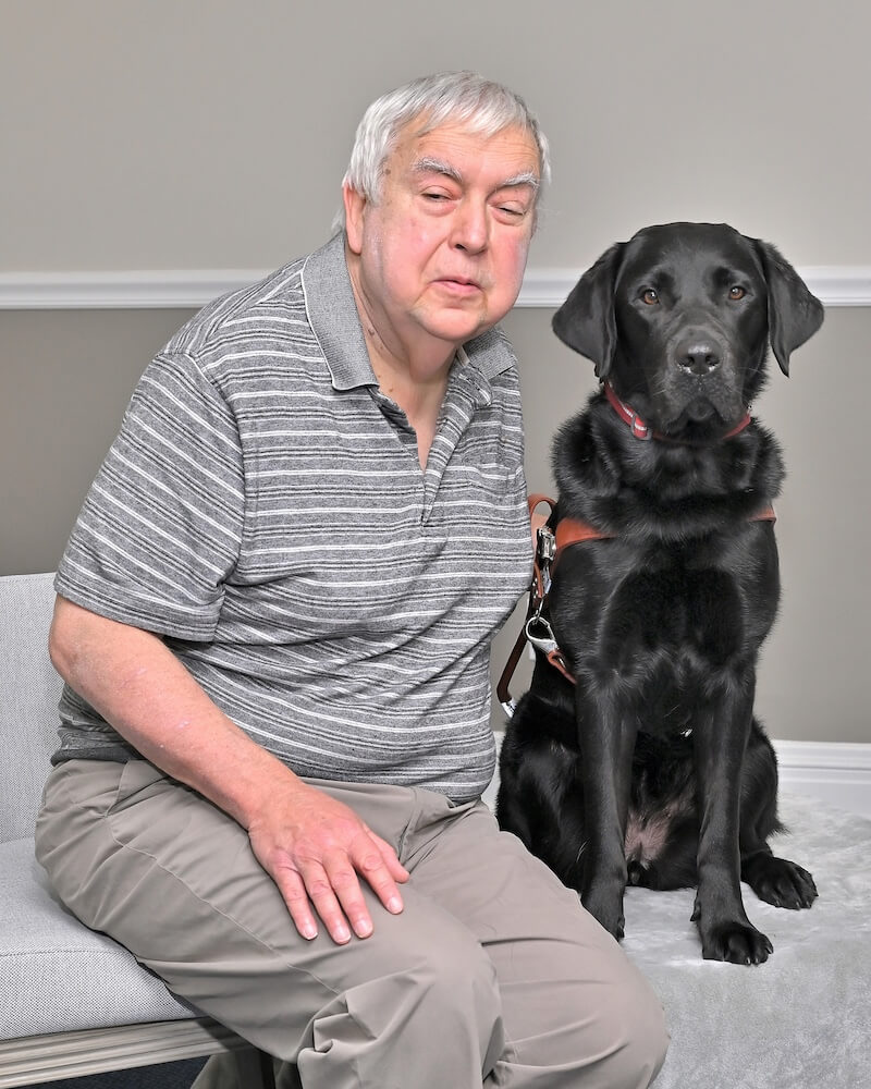 Brad sits next to black Lab guide dog Laurel for team portrait