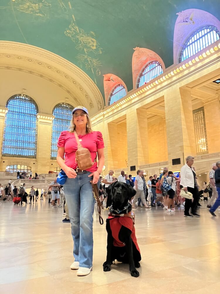 DeAnna stands with black Lab guide dog Whimsey in Grand Central