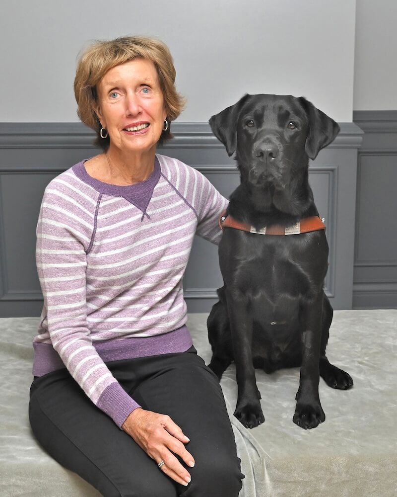 Gail sits next to black Lab guide dog Danielle for team portrait