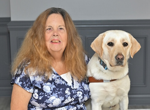 Kim sits with yellow lab guide dog Amaya for team portrait