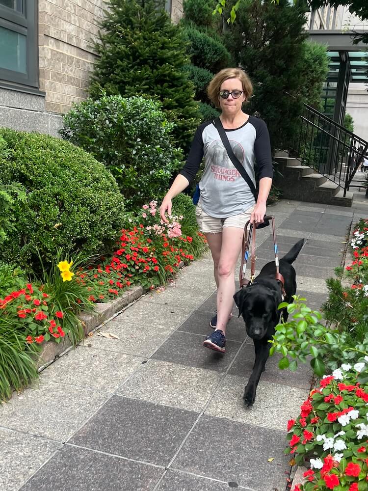Margot and Jennifer walk quickly between red flowers and plantings 