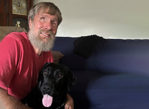Teddy has arm around black Lab guide Dan while sitting on a couch for team portrait