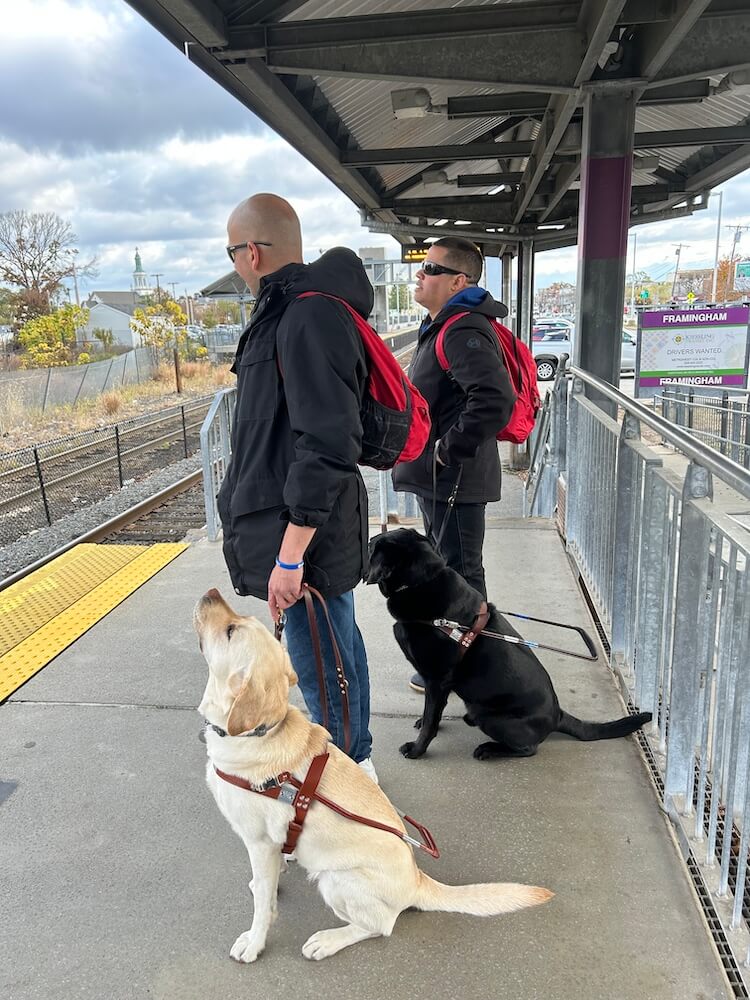 John and Adele stand on train platform with interpreter & graduate William with Kendall