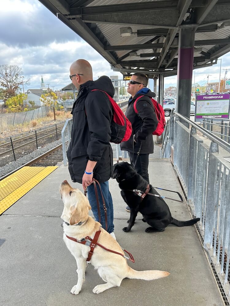 John and Adele stand on train platform with interpreter & graduate William with  Kendall