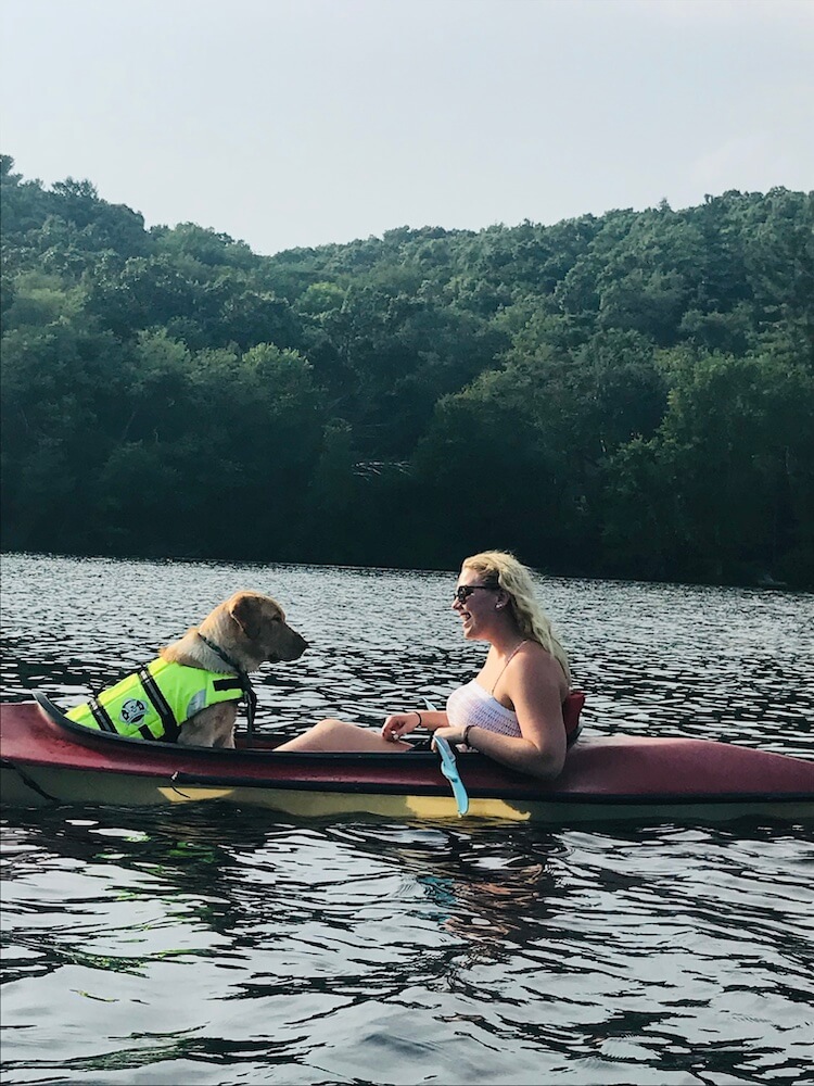Pepper kayaking with raiser Morgan on dark blue water across from a wooded area