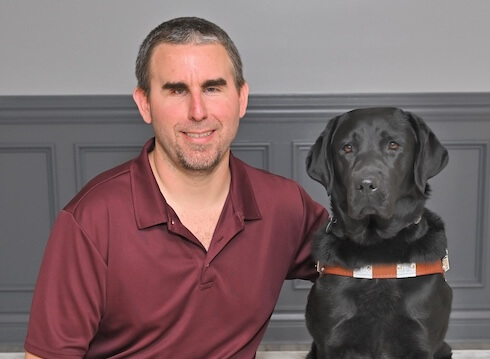 Tommy sits with black Lab guide dog Eva for their graduate portrait