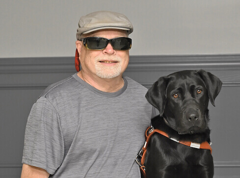 James sits next to black lab guide dog Peony for their formal guide dog portrait