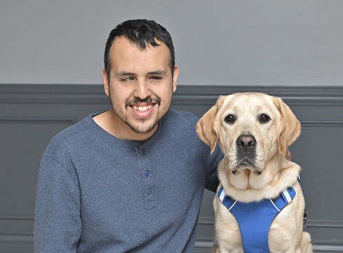 Brayan sits next to yellow Lab guide Macro for their graduate team photo