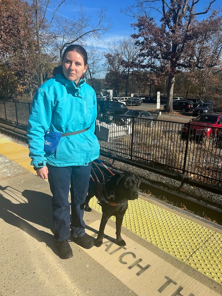 Candice walks safely on the sunny train platform  with Charlotte between here and the edge