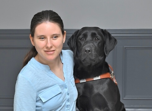Candice sits next to black Lab guide Charlotte for their graduate team photo