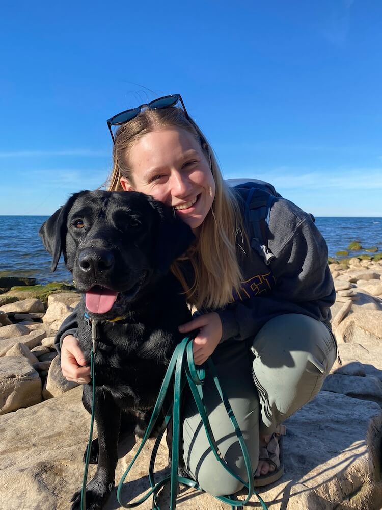 Black pup Elliott with raiser Jess on sunny seaside rocks