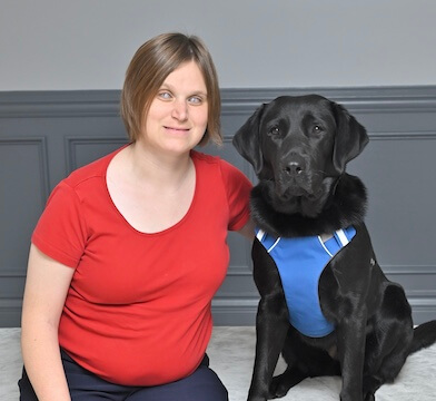 Kira leans towards black Lab guide Kona as they sit side by side for team portrait