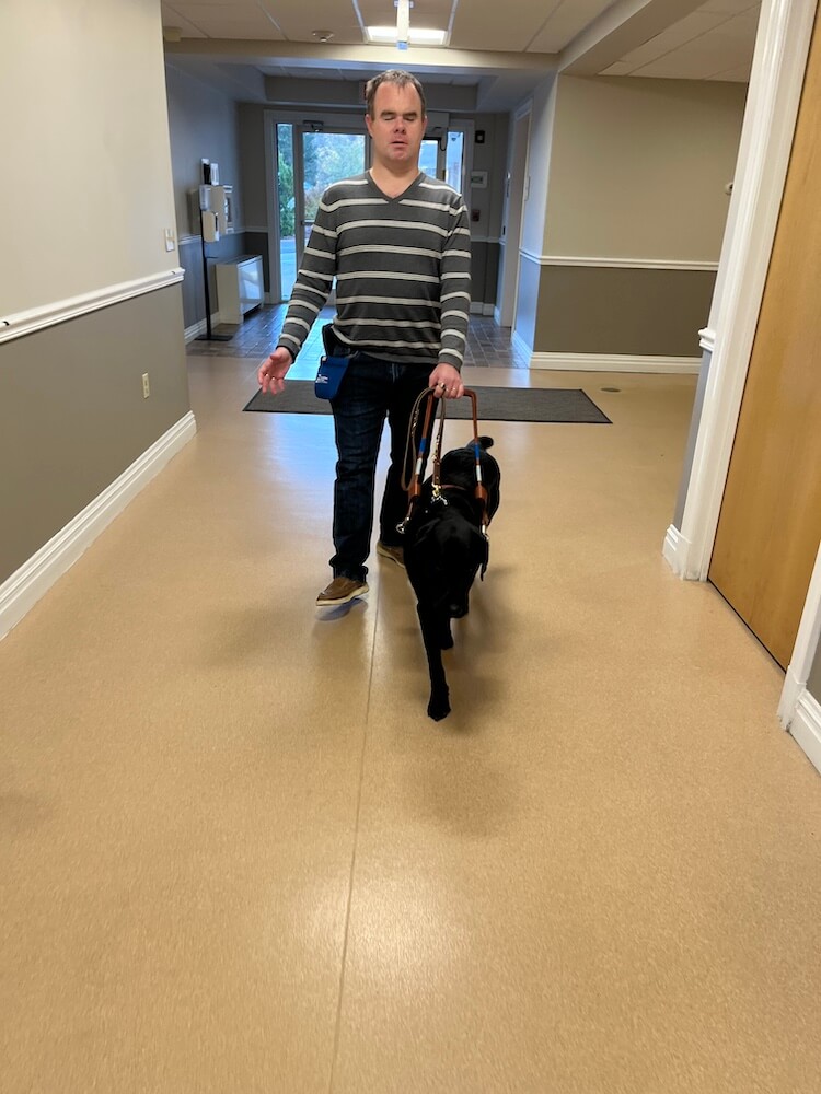 Michael and black Lab guide dog Emerson walk safely down hallway in Training School