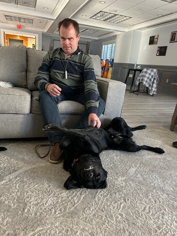 Michael sits on couch while petting guide dog Emerson's   belly
