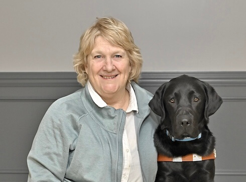 Claire sits with black Lab guide dog Vero for their team portrait