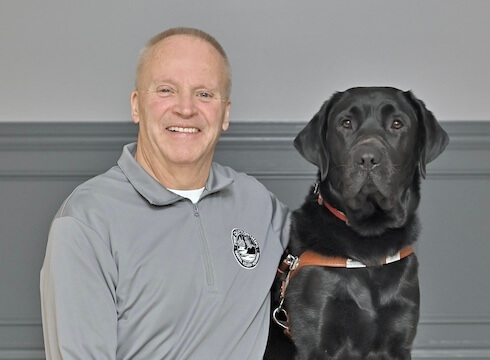 Greg and his black lab guide dog Vern sit together for their team portrait
