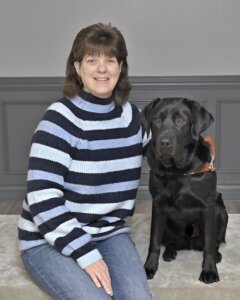 Julie sits next to black Lab guide Flyer for their team portrait