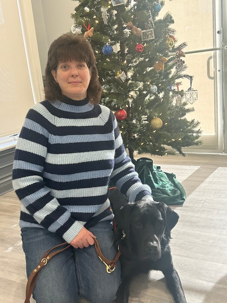 Julie and black lab Flyer pose next to Training School Christmas tree