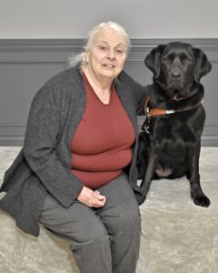 Laurie and black lab guide dog Fay sit together for their team portrait