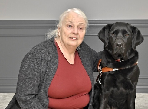 Laurie and black lab guide dog Fay sit together for their team portrait