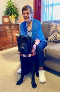 Marcie sits in her home with black Lab guide dog Kobe sitting between her feet