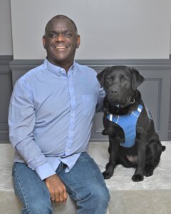 Renard sits next to black Lab guide Krissy for their graduate team photo