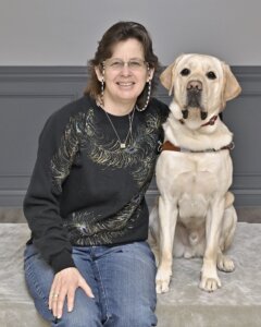 Stacy sits next to yellow Lab guide Vancouver for their team portrait