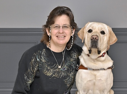 Stacy sits next to yellow Lab guide Vancouver for their team portrait