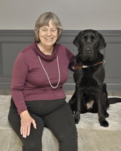 Veronica sits with arm around black Lab guide dog Lacy for team portrait