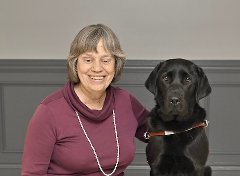 Veronica sits with arm around black Lab guide dog Lacy for team portrait