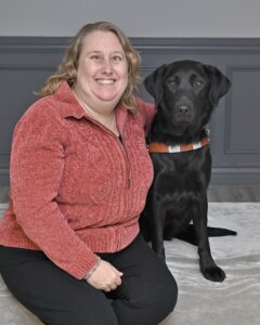 Angela sits with black Lab guide dog Havana for their team portrait