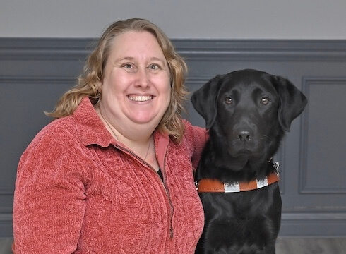 Angela sits with black Lab guide dog Havana for their team portrait