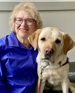 Gail sits next to yellow Lab guide dog Journey for their team portrait
