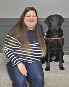 Melissa sits with black Lab guide dog Catalina for their team portrait