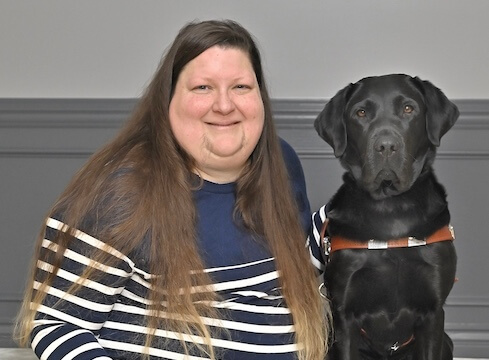 Melissa sits with black Lab guide dog Catalina for their team portrait