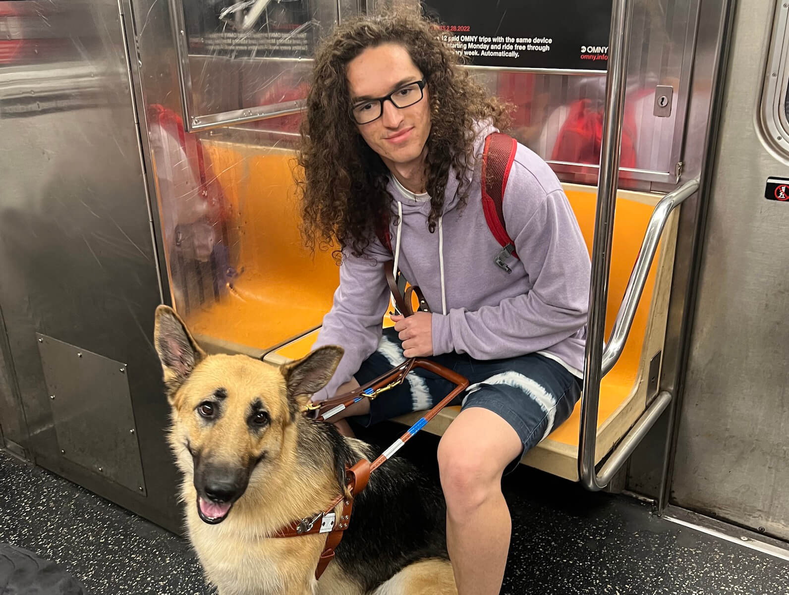 Young male graduate sits on subway with German Shepherd guide in front of him