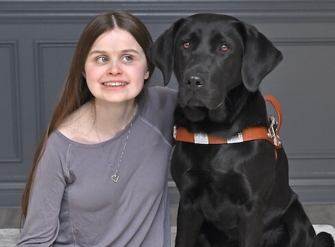 Caitlyn sits with black Lab guide dog Rory for their team portrait