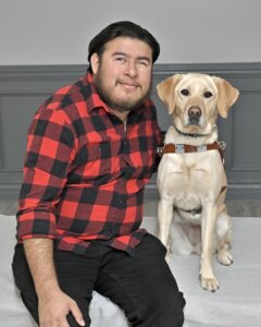 Fernando is next to yellow Lab guide dog Millie as they sit for their team portrait