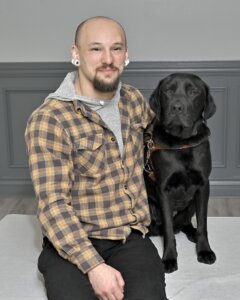 Lukas sits with black Lab guide dog Sawyer for their team portrait